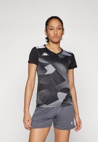 T-shirt de sport noir avec des motifs blancs dynamiques, à manches courtes et en col en V. Associé à un short gris.
