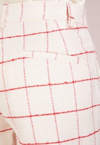 Pantalons en tissu tissé blanc avec un motif de grille rouge, présentant une taille haute et des poches latérales. Surface texturée avec un design structuré.