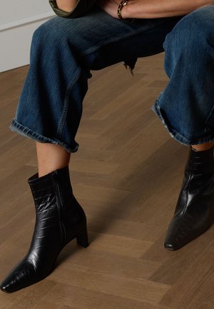 Zwarte enkellaarsjes van leer met een puntige neus, een krokodillenreliëf, een ritssluiting aan de zijkant en een lage blokhak, gedragen met cropped denim.