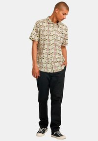 Short-sleeve beige shirt with a colorful floral pattern, paired with black pants and black sneakers. The shirt features a button-down collar.