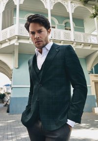 Ciemnozielony marynarka w kratę z klapami, na dwa guziki i kieszenią na piersi. Pod spodem biała koszula, uzupełniona szarymi spodniami garniturowymi.