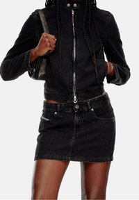 Zwarte spijkerjasje met een hoge kraag en ritssluiting aan de voorkant, gecombineerd met een zwarte spijker minirok. Voorzien van zakken aan de voorkant en metalen accenten.