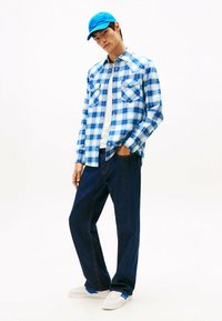 Blauw-wit geruit overhemd, wit T-shirt, donkerdenim broek en blauwe pet. Casual sneakers met blauwe accenten. Heeft borstzakken.