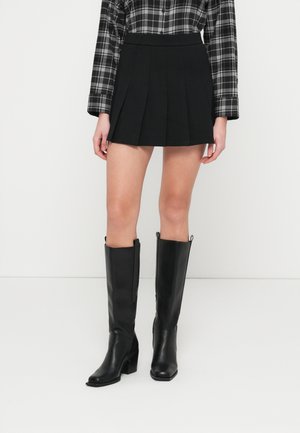 Svart plissert miniskjørt kombinert med en svart og grå rutete skjorte med lange ermer. Fottøyet består av knelang svarte lærstøvler med tykke hæler.