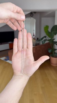 Strieborný reťazec držaný v ruke, s predĺženými článkami a hladkou textúrou, zobrazený na neutrálom vnútornom pozadí.