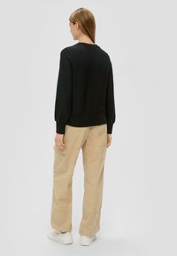 Zwarte sweatshirt met een ronde hals, geribbelde mouwen en zoom. Gecombineerd met beige cargobroek met zijzakken en een relaxte pasvorm. Witte sneakers.