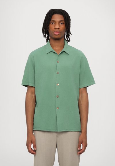 Camisa verde de manga corta hecha de tejido texturizado, con collar, botones en la parte delantera y un corte relajado.