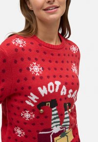 Suéter de punto rojo con festivos patrones de copos de nieve y lunares, con el texto "NO SOY UN PAPÁ NOEL", acentos a rayas verdes y negras, y cascabeles dorados.