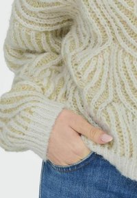 Cremfarbener gestrickter Pullover mit einem strukturierten Zickzackmuster, versehen mit breiten, gerippten Bündchen und einem weichen, flauschigen Finish, kombiniert mit Jeans.