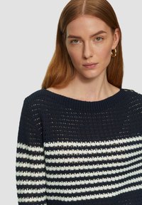 Dunkelblauer gestrickter Pullover mit einem gestreiften Design in weiß, offenem Webmuster und rundem Ausschnitt. Auffällige Knopfakzente an den Schultern.