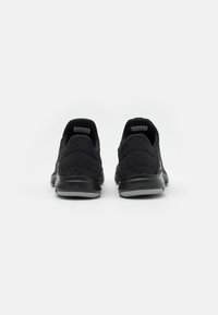 Baskets noires de sport avec une tige en tissu texturé, un dos rond et une semelle en caoutchouc. Présente un design minimaliste sans logos ni éléments métalliques visibles.