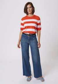 Red and pink striped short-sleeve knit top, high-waisted wide-leg blue denim jeans, black belt, and light blue frayed slide sandals.