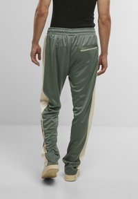 Grüne Trainingshose mit cremefarbenen Seitenpaneelen, aus strukturiertem Material und mit elastischem Bund. Enthält ein kleines Detail mit einer Gesäßtasche.