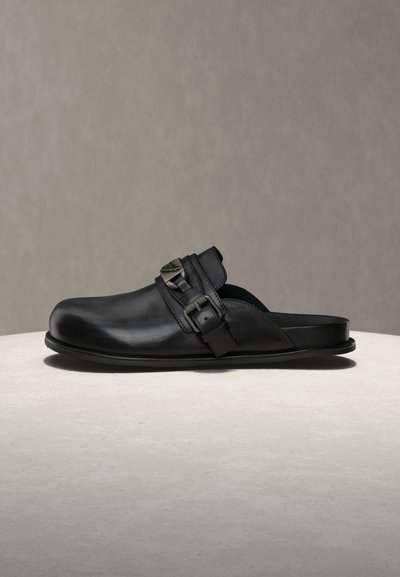 Μαύρο δερμάτινο κλογκ χωρίς κορδόνια με στρογγυλεμένη μύτη και δύο ρυθμιζόμενες αγκράφες σε φαρδιά λωρίδα στον πάνω μέρος του ποδιού, εμφανίζεται σε ανοιχτή επιφάνεια.