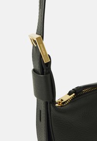 Black leather bag strap features a gold-tone metal clip with an embossed logo. Soft texture with a zip closure. Minimalistic design elements.