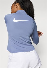 Nike Langarmshirt aus hellblauem Stoff mit hohem Kragen. Mit einem weißen Logo auf der Rückseite, einem abgerundeten Saum und strukturiertem Finish.