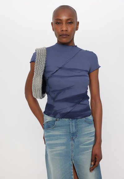 Mørkeblå tætsiddende top med ribbet tekstur og asymmetrisk design, parret med lyseblå denim nederdel med en frontslids. Accentueret med en perlebesat rem.