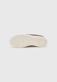 Baskets vertes avec une tige en toile texturée, semelle en caoutchouc crème, motif de semelle circulaire et détail de marque subtil sur la semelle.