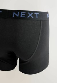 Boxer de algodón negro con una cinturilla ancha negra que presenta la marca "NEXT" en azul. Textura suave y diseño ajustado.