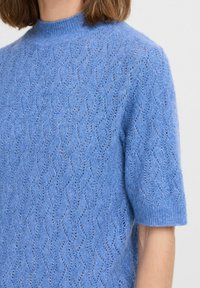 Hellsblaues kurzärmliges Sweatshirt aus strukturiertem Strickstoff, mit einem wellenförmigen Muster und einem gerippten hohen Kragen.