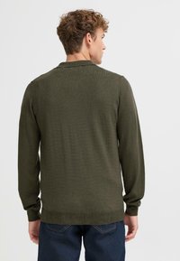 Pullover a maglia verde scuro, a maniche lunghe, con una texture liscia e orlo a coste. Presenta un colletto classico e un design a taglio dritto.