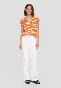 Losse oranje en witte gestreepte top met een V-hals, gecombineerd met witte wijde broek en zwarte sandalen. Gladde textuur en casual ontwerp.