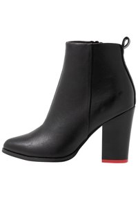 Schwarze Knöchelstiefel aus strukturiertem Leder, mit einer spitzen Zehe, hohem Blockabsatz und einem roten Akzent am unteren Ende des Absatzes.