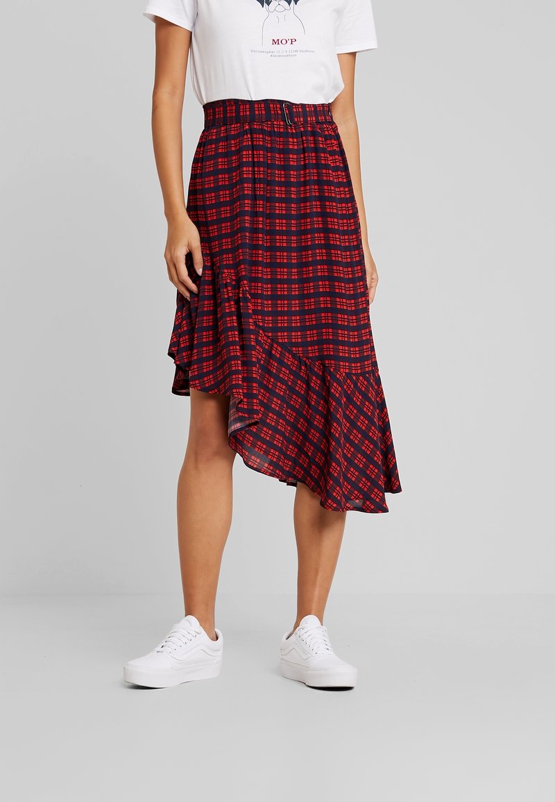 Rood en marineblauw geruite rok met een asymmetrische zoom, gemaakt van lichte stof, gathered taille, gecombineerd met witte sneakers.