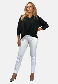 Czarna, luźna bluzka z dekoltem w kształcie litery V i rękawami o długości trzech czwartej, w połączeniu z białymi, dopasowanymi spodniami. Szpilki w print węża.