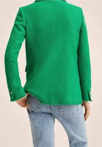 Zielona kurtka z teksturowanej tkaniny, z długimi rękawami, z wykończeniami z srebrnych guzików przy mankietach i dopasowanym krojem. Widok z tyłu.