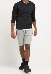 Black Nike sweatshirt with a front pocket and logo; paired with gray Nike shorts featuring an elastic waistband and cuffed hems.