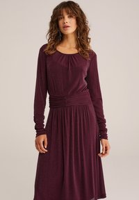 Rochie cu mâneci lungi, guler rotund, până la genunchi, într-o nuanță de burgund profund, cu o strălucire subtilă, având talie elastică și o fustă fluidă.
