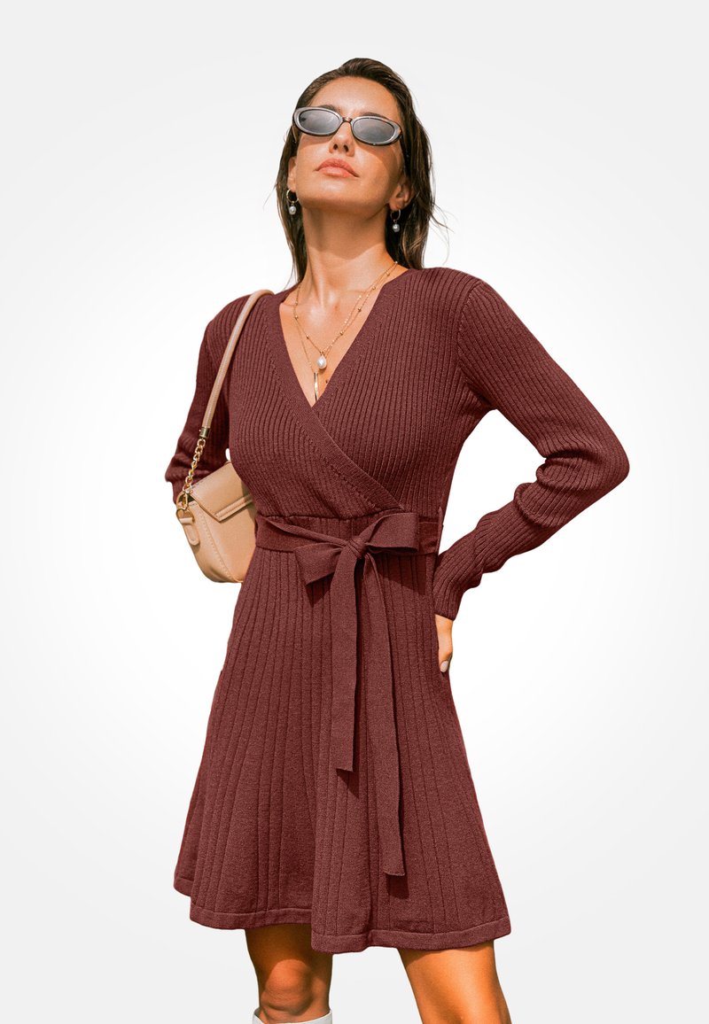 Vínová žebrovaná pletená zavinovací šaty s dlouhými rukávy a zavazovacím páskem. Má V-krk a rozšířený lem. Na sobě má neutrální doplňky.