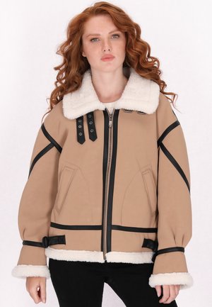 Beige Jacke mit schwarzem Besatz und Lammfellkragen. Verfügt über einen Reißverschluss vorne, zwei Seitentaschen und verstellbare Riemen am Saum und an den Manschetten.