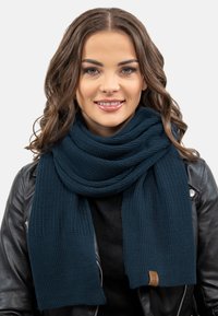 Dunkelblaut gerippter Strickschal mit glatter Textur, lässig drapiert, mit einem kleinen Lederschild an einem Ende.