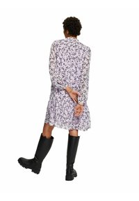 Vestido de estampado floral en lavanda claro con mangas largas translúcidas y un dobladillo en capas, combinado con botas de goma negras hasta la rodilla.