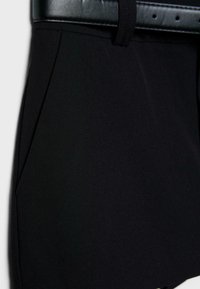 Gros plan sur un pantalon noir sur mesure avec une poche latérale et une boucle de ceinture en cuir noir passée dans la ceinture.