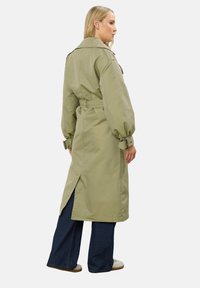 Długi, oliwkowozielony trencz z paskiem w talii, szerokimi ramionami, zapiętymi mankietami, bocznymi rozcięciami i gładką, teksturowaną powierzchnią.