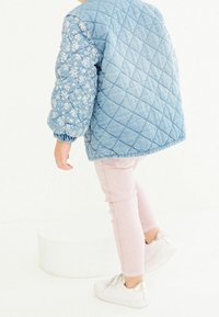 Quilted Denim-Bomberjacke mit floral gemusterten Ärmeln, kombiniert mit hellrosa Skinny-Jeans und weißen Sneakers mit metallischen Akzenten.
