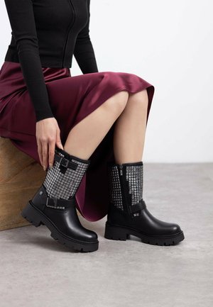 Botas negras con acentos plateados texturizados, con hebillas y una suela gruesa, combinadas con una falda de satén burdeos.