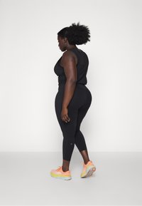 Top de entrenamiento negro y leggings, con un diseño ajustado. Llevado con zapatillas de correr coloridas, que muestran una mezcla de acentos naranjas y amarillos.