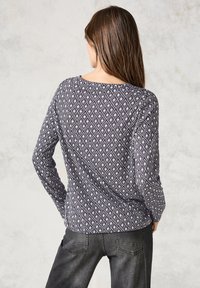 Haut à manches longues en motif géométrique bleu marine et blanc, avec un col rond et une coupe décontractée, associé à un jean gris foncé.