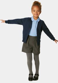 Cardigan blu navy, camicia con colletto blu, pantaloni grigi e collant grigi. Scarpe nere con un cinturino. Bambino in piedi con le braccia tese.