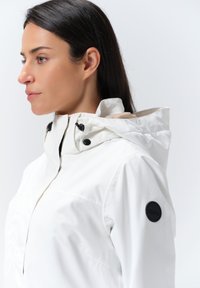 Weiße wasserdichte Jacke mit hohem Kragen, verstellbarem Kapuze und schwarzen Hardware-Akzenten. Sie verfügt über eine glatte Textur und ein minimalistisches Design.