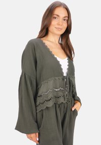 Olivgrüner Wickelcardigan aus strukturiertem Stoff, mit gewellten Spitzenbesätzen, langen Ärmeln und einer Taillenknotenverschluss.