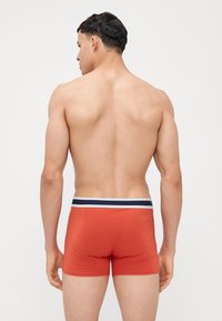 Boxer brevi rossi con una cintura a strisce blu e bianche. Realizzati in tessuto liscio ed elastico. Il design presenta una vestibilità attillata e uno stile a vita media.