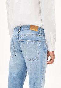 Lichtblauwe denim jeans met een rechte pasvorm, achterzakken en een beige label met "ARMEDANGELS" op de tailleband.
