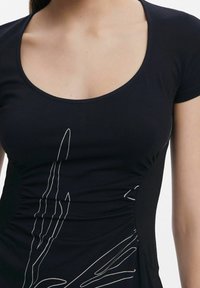 Haut noir à manches courtes avec un décolleté arrondi et des fronces sur les côtés. Présente des détails en art linéaire blanc sur le devant, offrant texture et contraste.