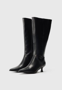 Μαύρες δερμάτινες μπότες μέχρι το γόνατο με μυτερή μύτη και μεσαίο τακούνι. Διαθέτουν λεία υφή και φερμουάρ στο εσωτερικό μέρος για κλείσιμο.