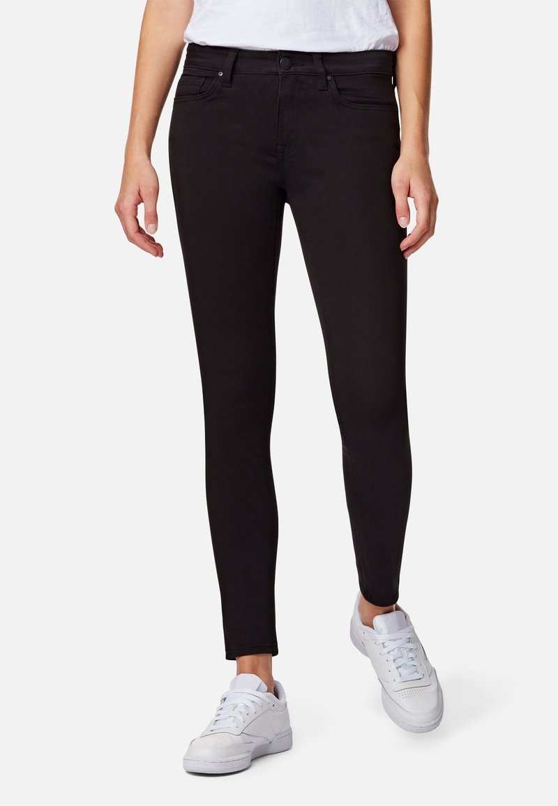 Jeans ajustados negros de mezclilla con una textura suave. Cinco bolsillos y pasadores para el cinturón; combinados con zapatillas blancas. Corte slim a lo largo de las piernas.